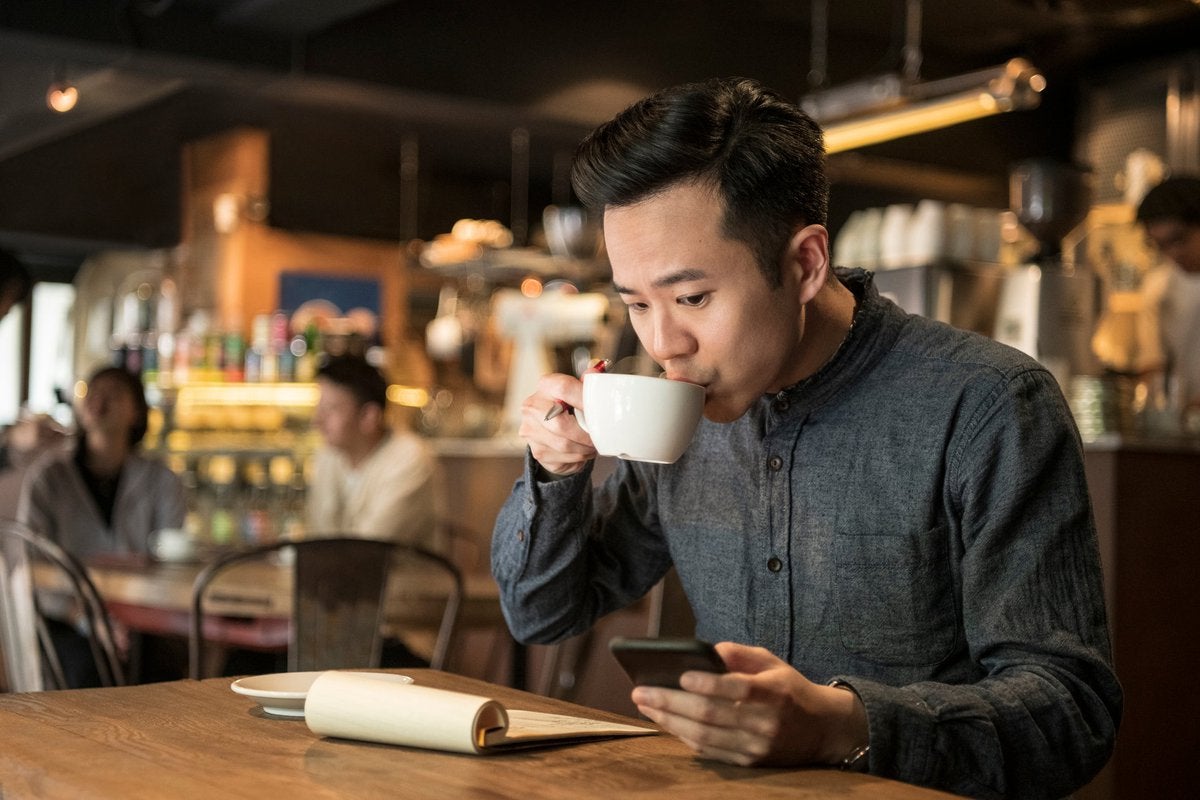 A young businessman is doing paperwork in the cafe and checking his phone.