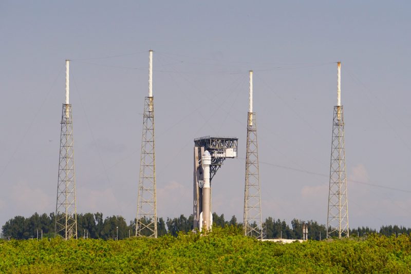 Boeing Starliner: A rocket and space capsule seen from behind 4 towers.